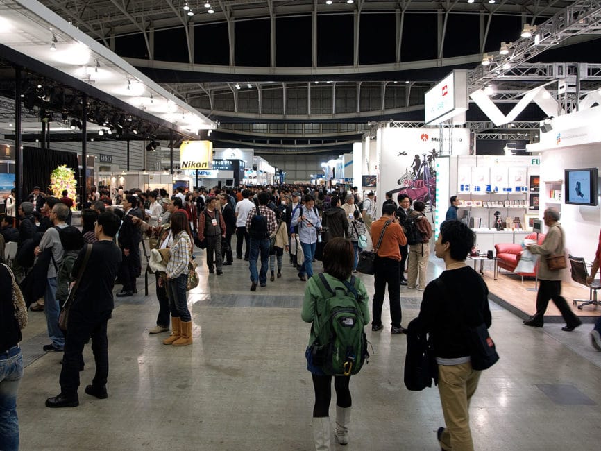 Crowded trade show floor with booths on left and right. 