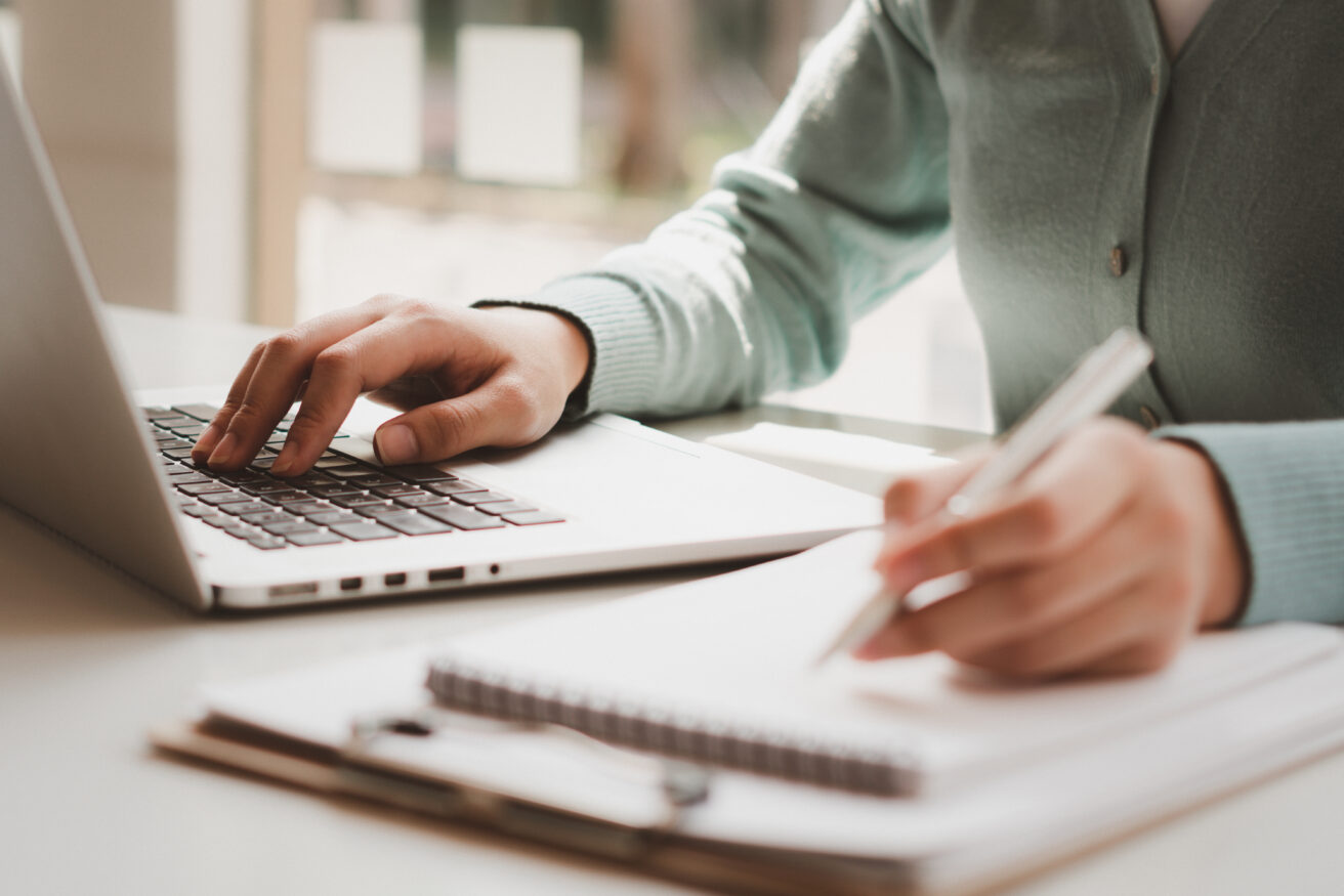 Businesswoman works on computer and write on notepad with pen 