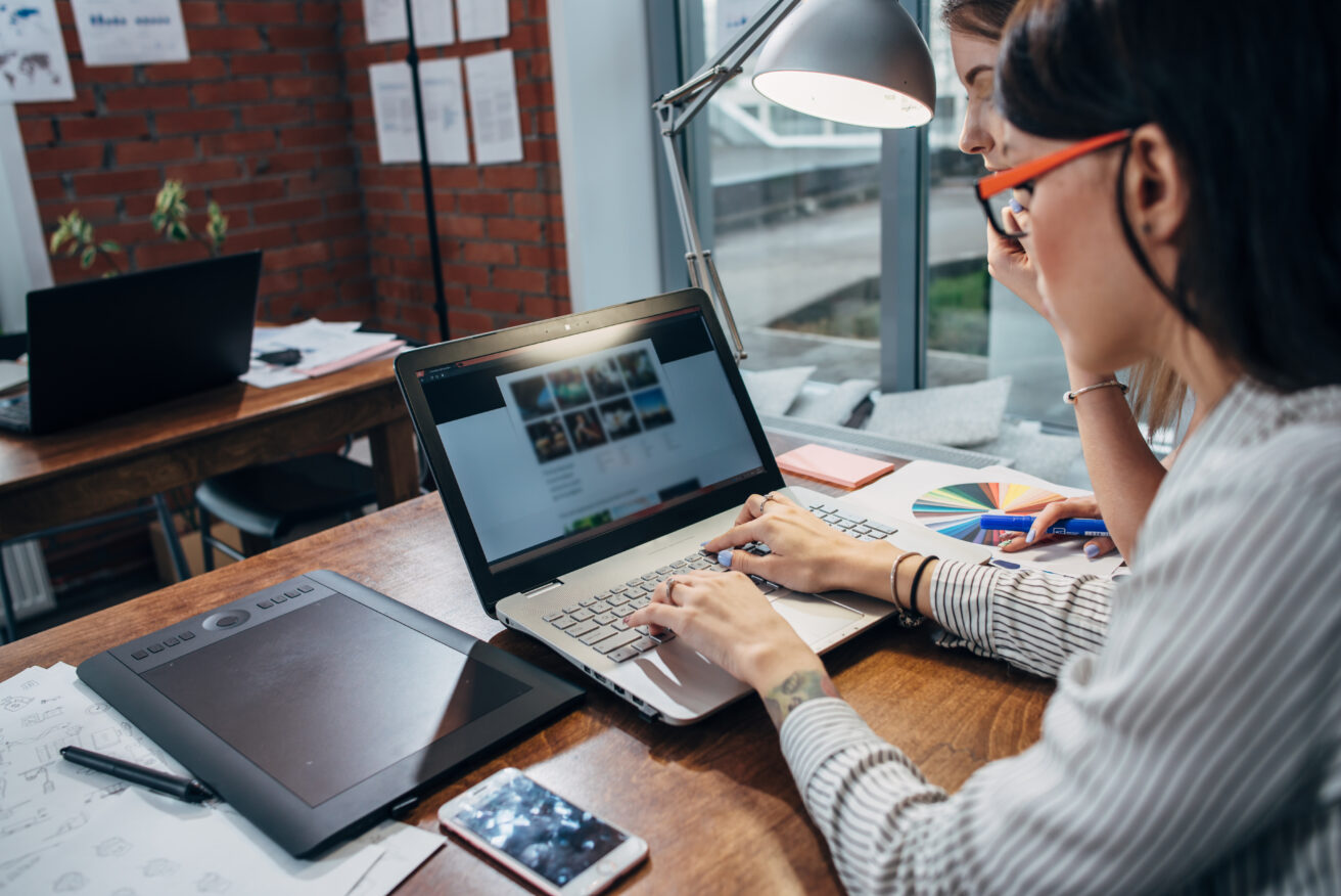 Two women working on new website design choosing pictures using the laptop surfing the internet.