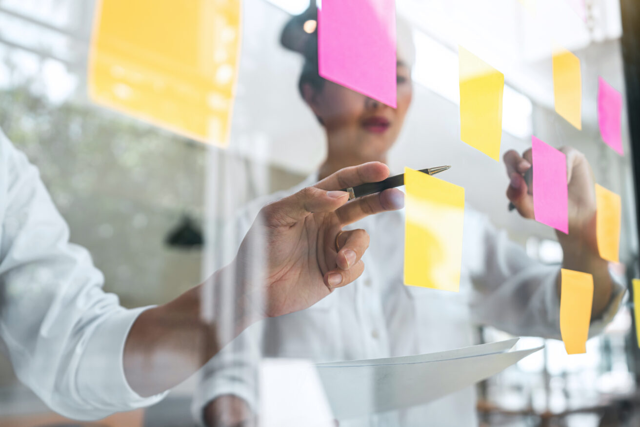 Young creative team professional using post it notes in glass wall to writing strategy business plan to development grow to success.