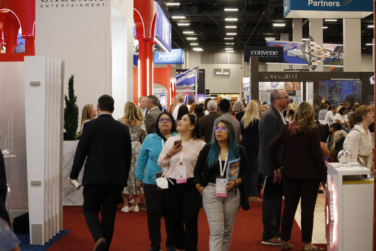 Group of diverse people walking through B2B event hall with various booths in the background