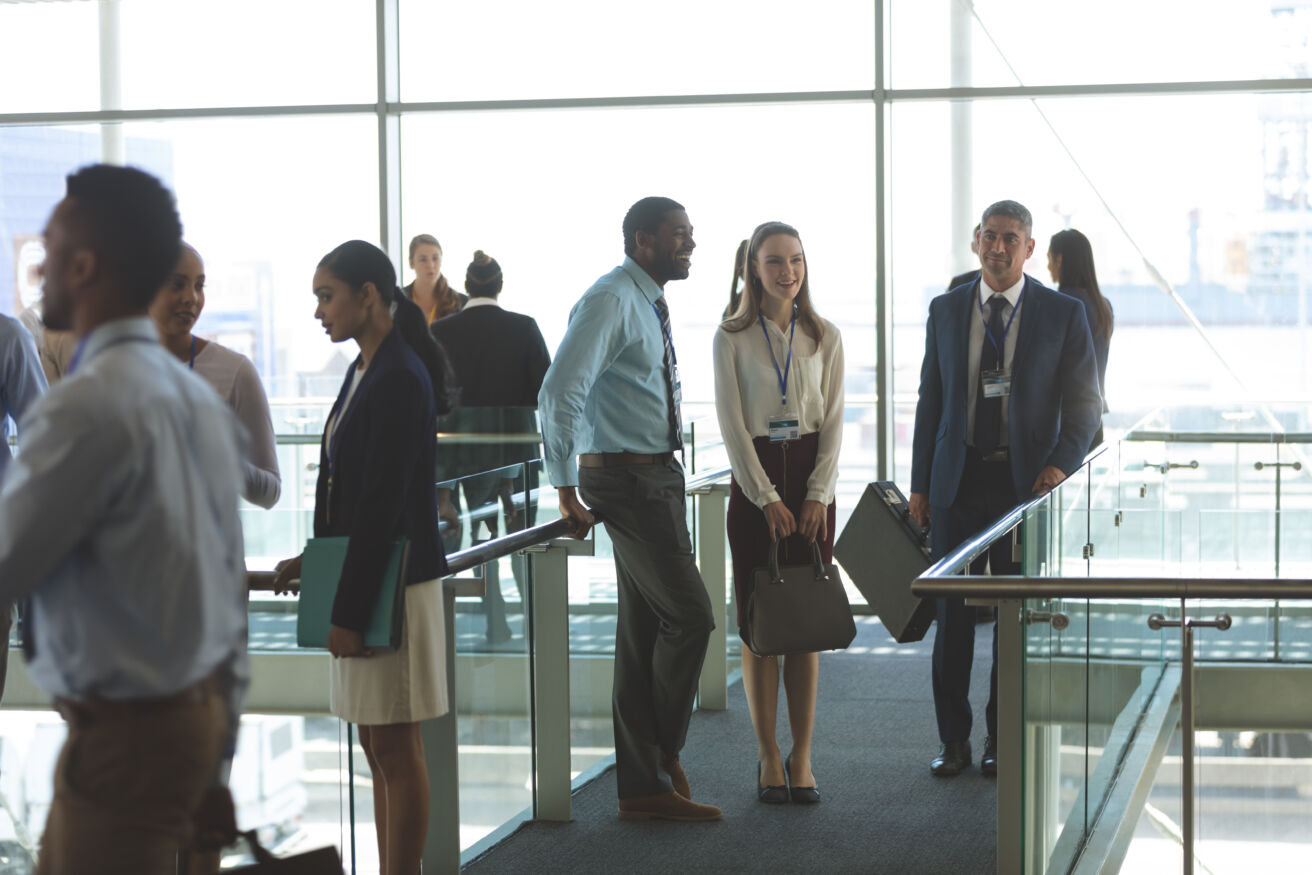 Group of diverse people in business attire standing in front of large windows conversing at an event